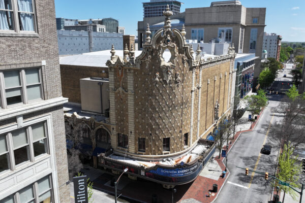 Ornate historic theater stands amid modern buildings on sunny day.