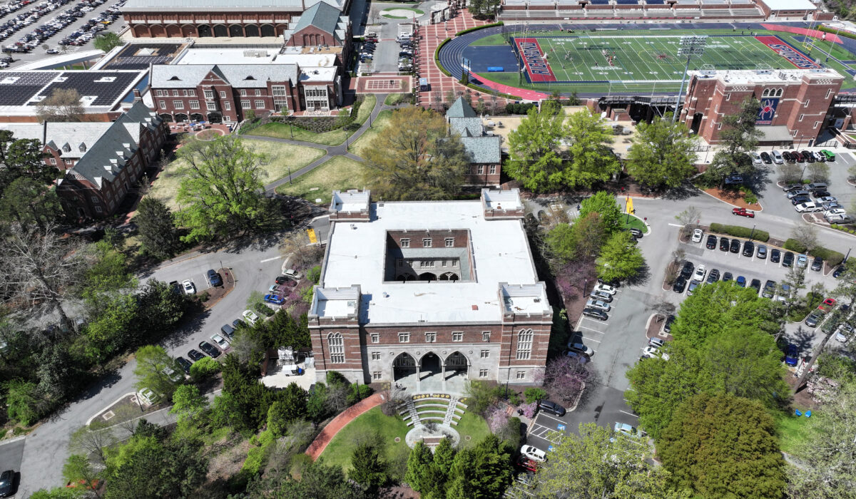 Aerial view of brick college building with trees and sports field.