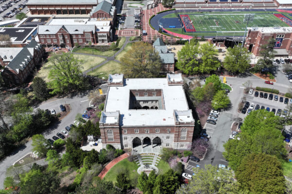 Aerial view of brick college building with trees and sports field.