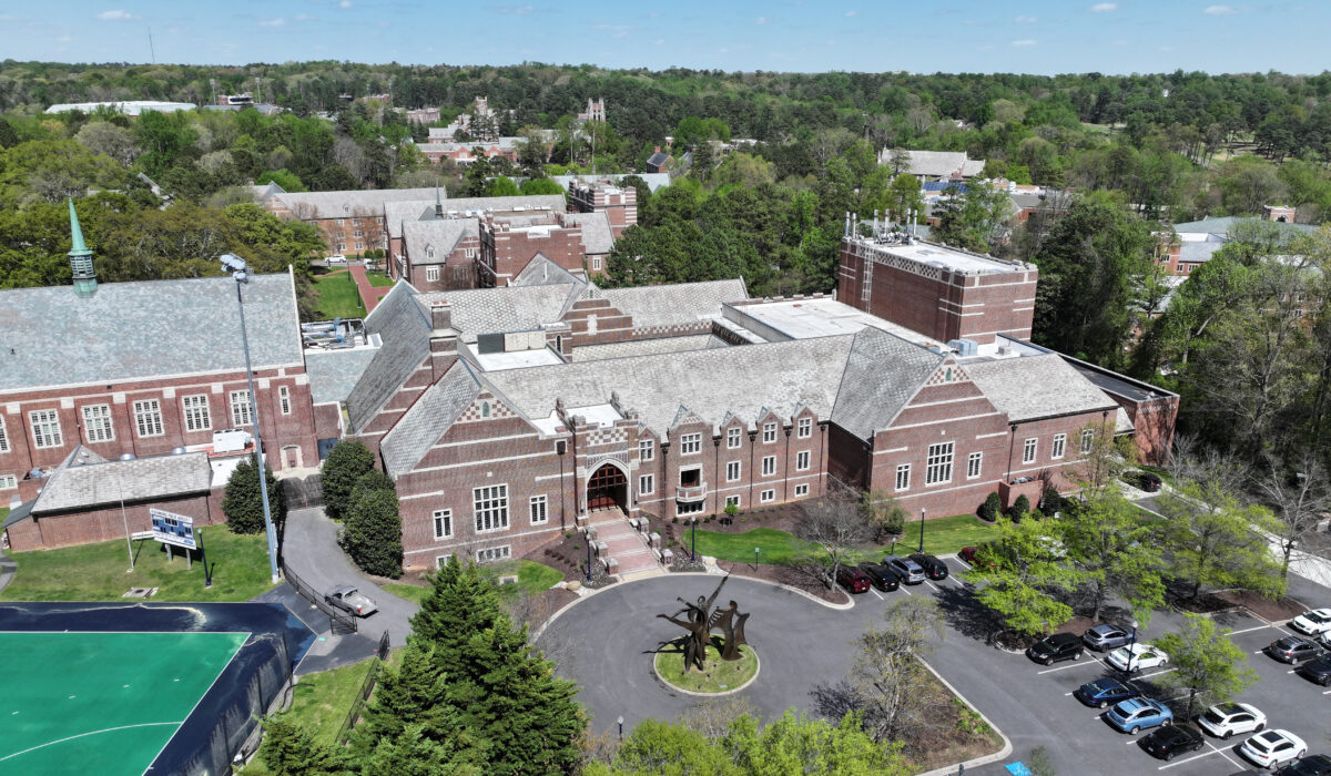 Aerial view: brick school, roundabout, cars, trees, nearby sports field.