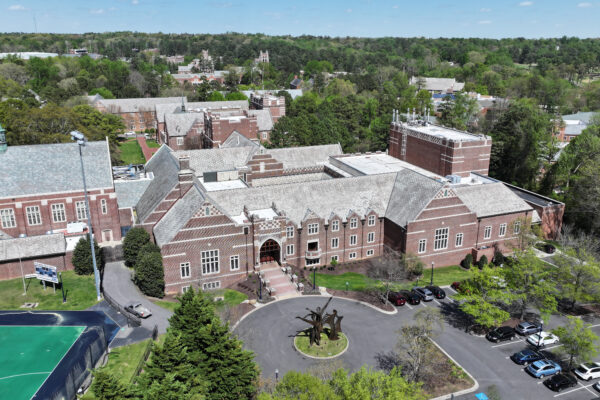Aerial view: brick school, roundabout, cars, trees, nearby sports field.