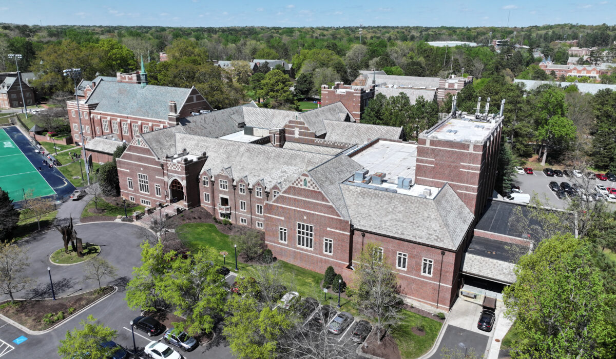 Aerial view: large brick school, peaked roofs, trees, sports field.
