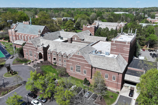 Aerial view: large brick school, peaked roofs, trees, sports field.