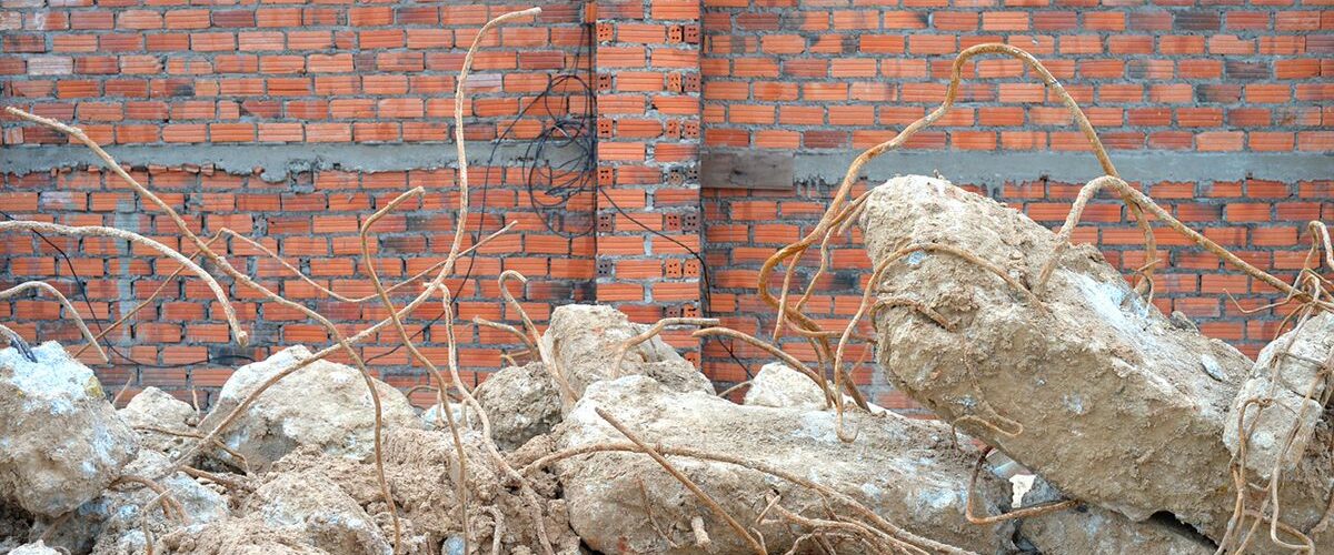 Broken concrete and rebar lie before a brick wall.