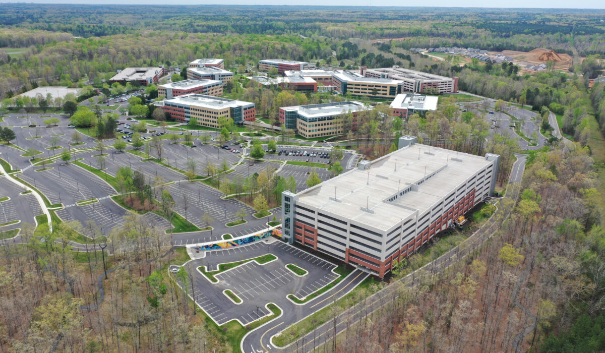 Aerial view: office complex, parking garage, trees, cloudy sky.