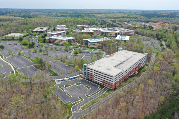 Aerial view: office complex, parking garage, trees, cloudy sky.