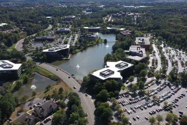 Aerial of office park: buildings, pond, cars, roads, trees.