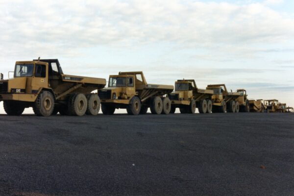 Heavy construction equipment parked on gravel under cloudy sky.