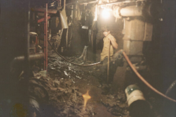 Person stands in dim, cluttered industrial space with muddy floor.