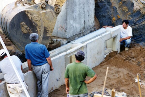 Four men use an excavator to position concrete blocks.