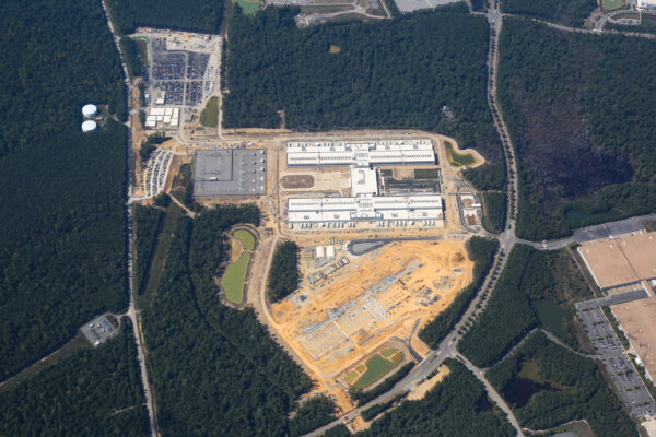 Aerial view: large complex with buildings, parking, construction, forest.