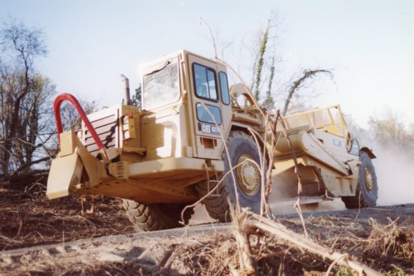 Yellow Caterpillar vehicle operates on dusty dirt site, debris around.