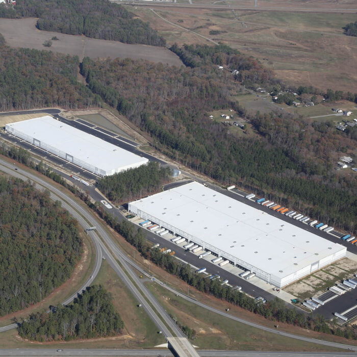 Aerial view: two large warehouses with loading docks, greenery.