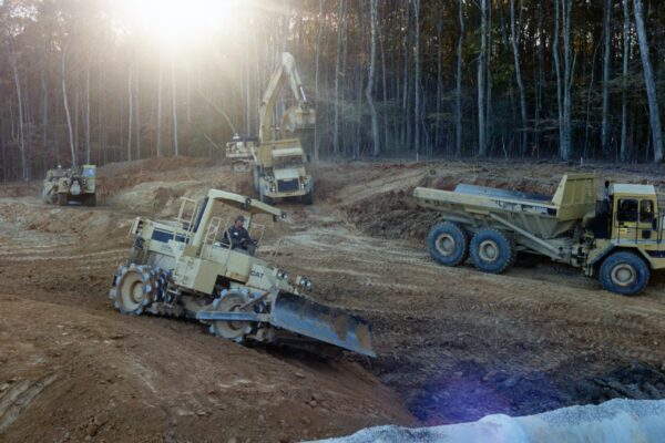 Bulldozer, excavator, and dump truck work on sunny dirt site.