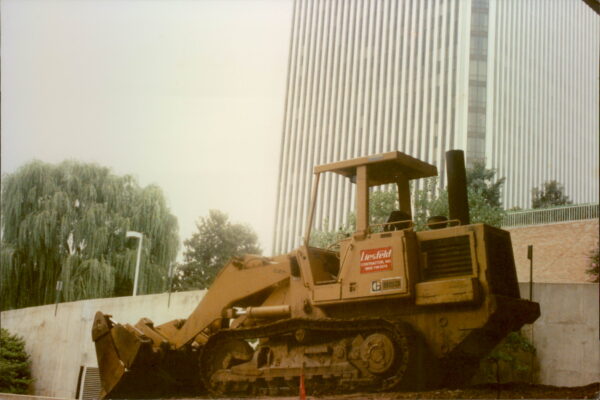 Yellow bulldozer parked on dirt near wall and buildings.