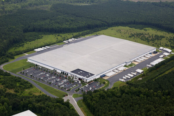Warehouse with parking, docks, and trucks in forested area.