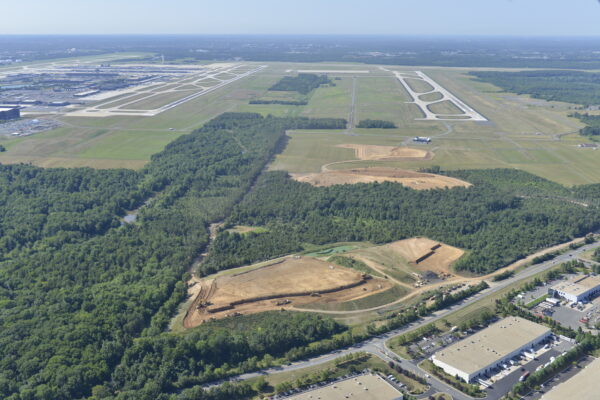 Aerial view: airport runway, cleared sites, forest, industrial buildings.