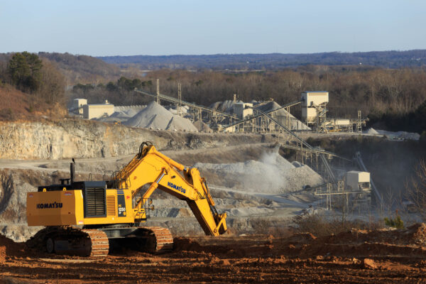 Yellow Komatsu excavator works at quarry with clear sky.