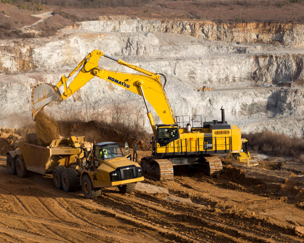 Excavator loads dirt into dump truck at open-pit mine.