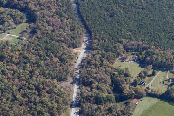 Aerial view: winding road through forest, fields, and warehouses.