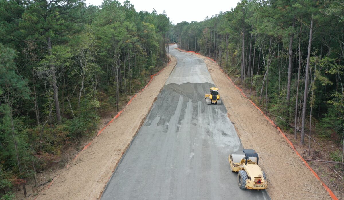 Aerial view: two road rollers on a tree-lined construction site.