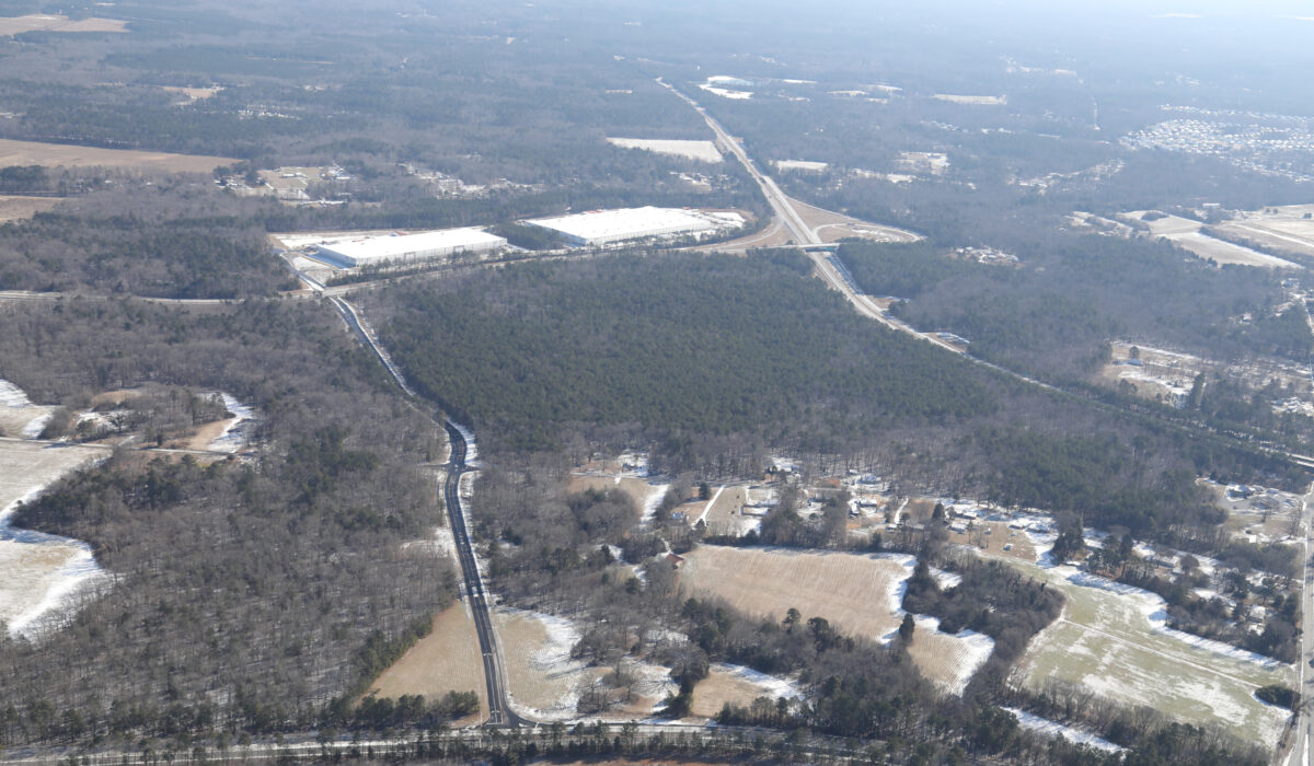 Aerial view of snowy rural land with roads and buildings.
