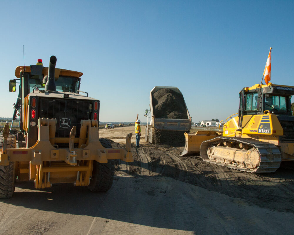 Dump truck unloads gravel between grader and bulldozer outdoors.