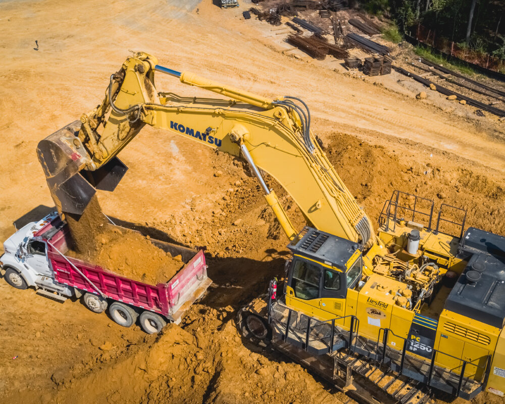 Yellow Komatsu excavator loads dirt into white and red dump truck.