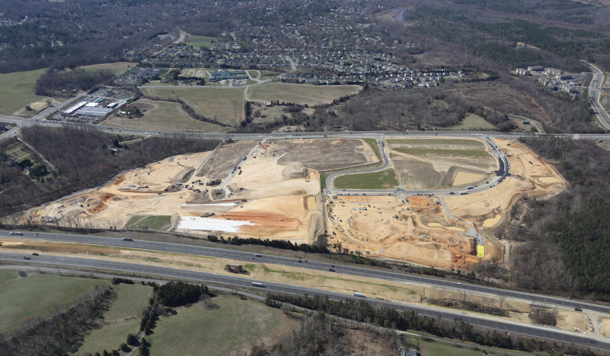 Aerial of large construction site amid roads, homes, and trees.