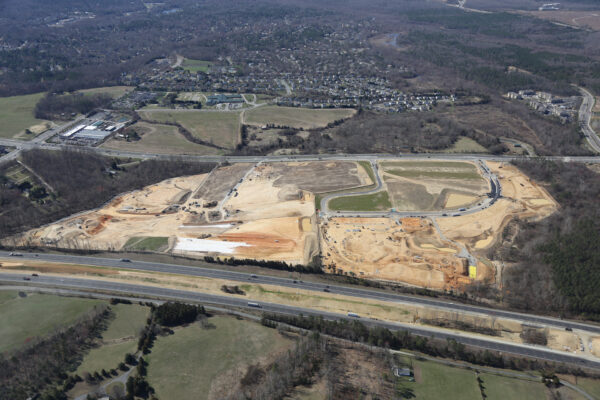 Aerial of large construction site amid roads, homes, and trees.