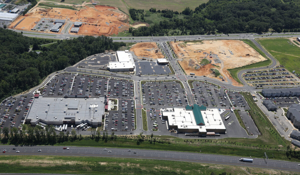 Aerial view: big shopping center, parking lots, forest, highway.