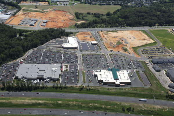 Aerial view: big shopping center, parking lots, forest, highway.