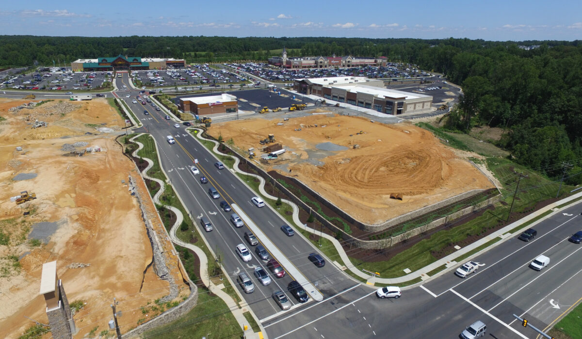 Aerial view of stores, parking lots, curving sidewalks, and cars on roads.