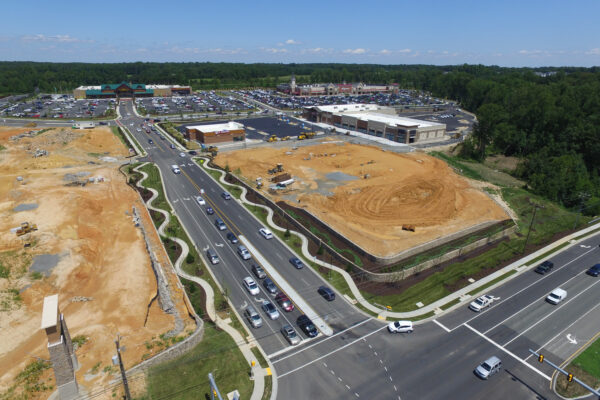 Aerial view of stores, parking lots, curving sidewalks, and cars on roads.
