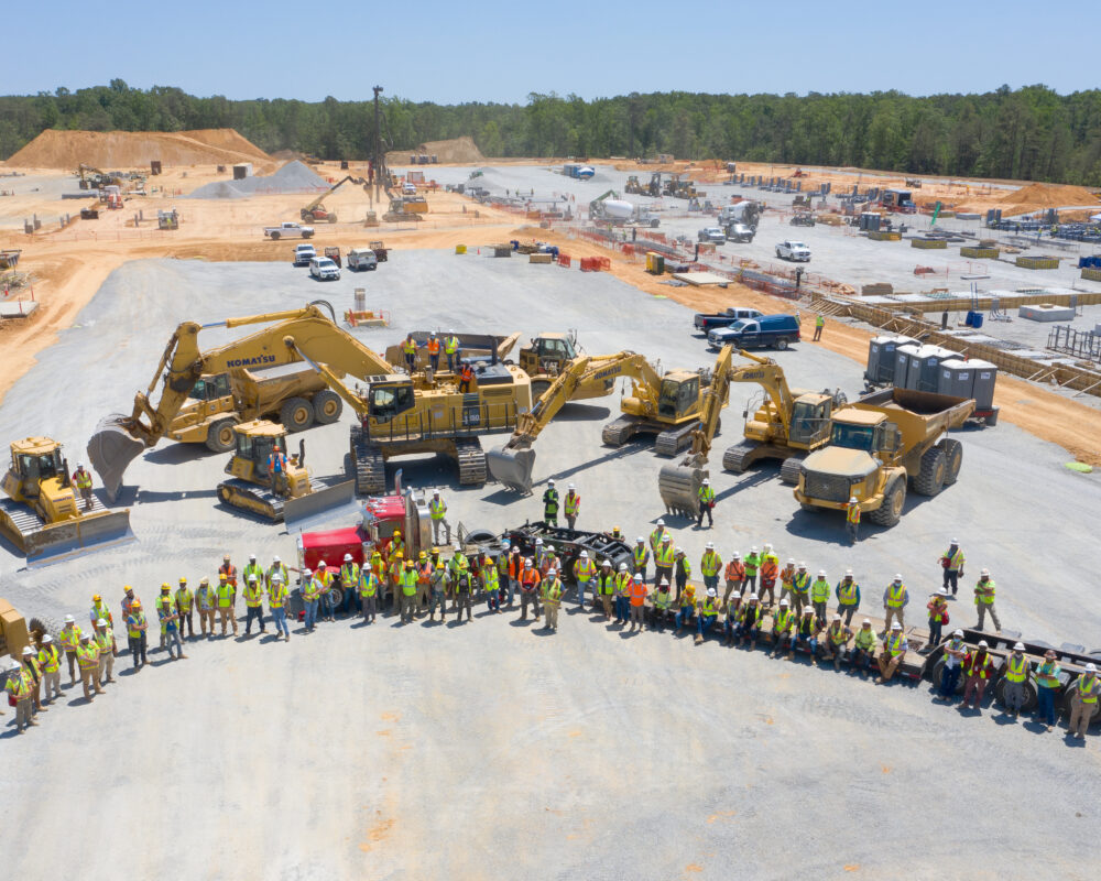 Construction workers in safety gear pose by machinery at site.