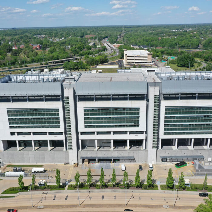 Aerial view: modern glass office building, trees, roads, parking.