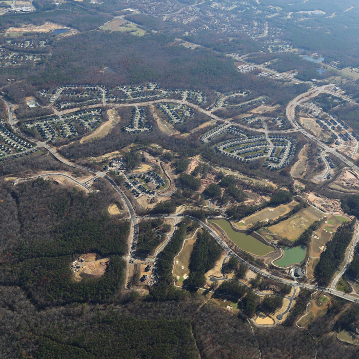 Aerial view of suburb: winding roads, homes, woods, ponds.