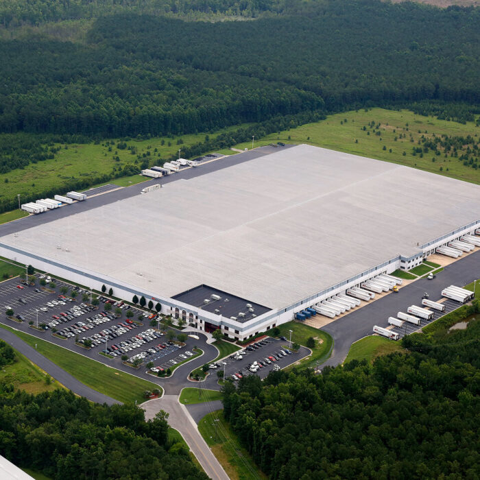 Aerial view: warehouse, parking lot, trucks, and surrounding forest.