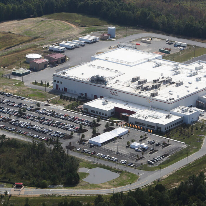 Aerial view of industrial facility with white roof and trucks.