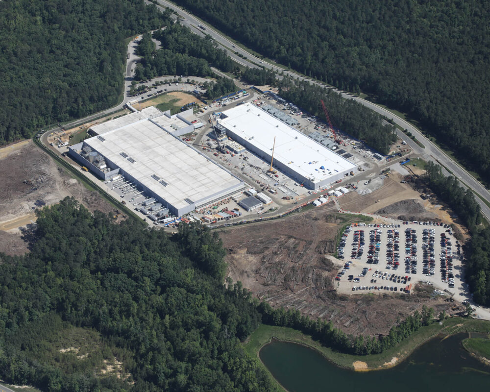 Aerial view of two white-roofed buildings with parking, forest.