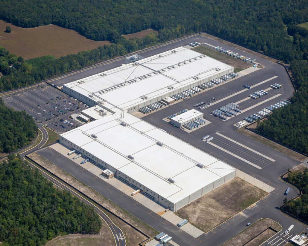 Aerial view of large warehouse, trucks, parking, and trees.
