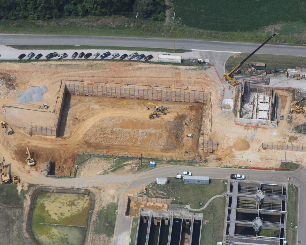 Aerial view: construction site with vehicles, cranes, materials, cars.