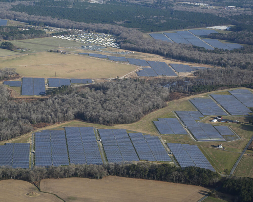 Aerial view of large solar panels among fields and forests.